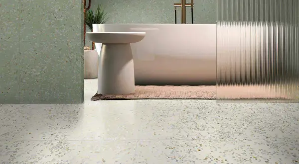 Baño moderno con bañera exenta y grifería dorada, sobre suelos de terrazo claros y paredes con el mismo acabado en tono verde.