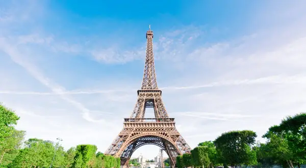 La icónica Torre Eiffel, un ejemplo del estilo arquitectónico de la época, se alza majestuosa bajo un cielo azul con nubes dispersas.