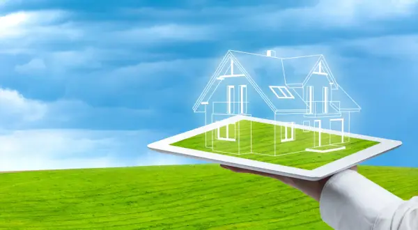 Diseño de una casa ecológica autosuficiente proyectada sobre una tablet, con un paisaje verde y cielo azul de fondo.