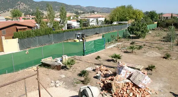 Terreno con materiales para construir dos casas. Se ven ladrillos, cementera y una excavadora.