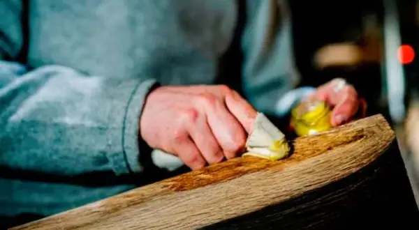 Manos aplicando cera a un trozo de madera. El proceso de **decapar madera** revela su belleza natural.
