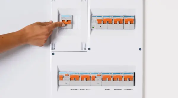 Panel de circuitos vivienda con interruptores naranjas. Una mano activa uno de los interruptores.