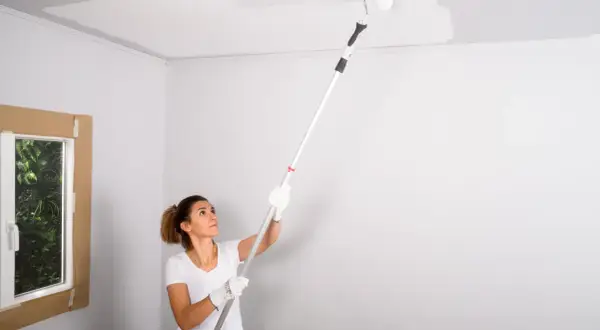Mujer pintando el techo con rodillo. La pregunta de si que se pinta primero el techo o las paredes es clave en esta tarea.