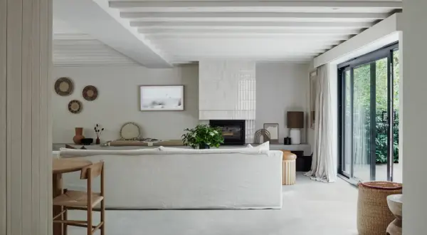 Salón moderno con suelo de porcelánico que es perfecto para crear un ambiente sereno. Sofá blanco, chimenea y grandes ventanales.
