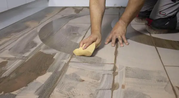 Man limpiando suelo porcelánico después de obra con una esponja, eliminando restos de cemento y polvo.