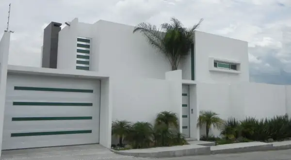 Casa moderna con líneas limpias y un estilo arquitectónico minimalista. Puerta de garaje blanca con detalles verdes.