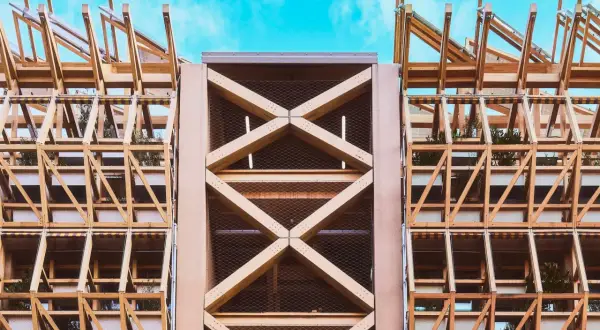 Estructura de madera con celosías y plantas, mostrando elementos de arquitectura moderna contra un cielo azul.