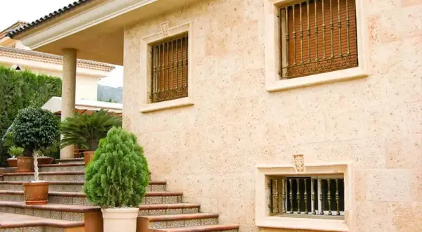 Fachada de casa con escaleras y plantas. Los distintos tipos de pared de piedra y detalles ornamentales resaltan la arquitectura.