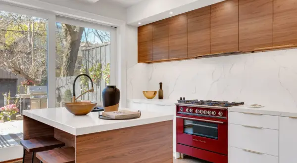 Cocina moderna con isla central, encimeras de cuarzo, gabinetes de madera y estufa roja. Un ejemplo de diseño de espacios interiores funcional y elegante.