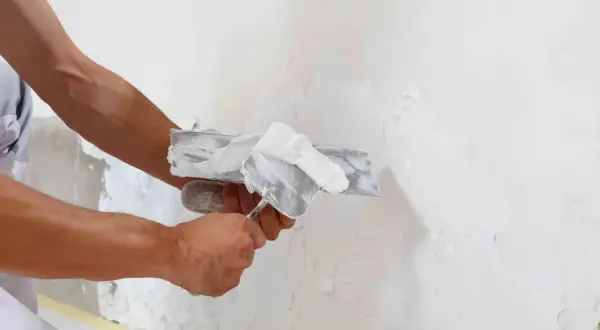 Man aplicando yeso a una pared con una llana, mostrando la diferencia entre enfoscado y guarnecido.