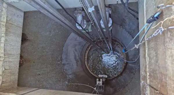 Vista superior de una estación de bombeo con tuberías y cadenas. El agua turbulenta llena el pozo, parte de la red de evacuación de aguas residuales y pluviales.
