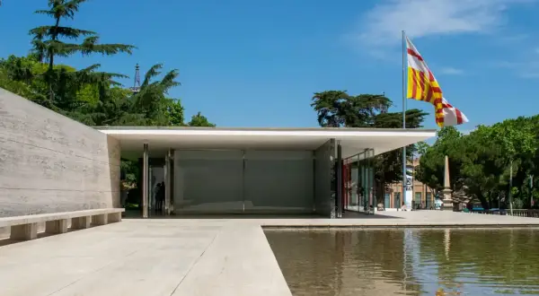 Pabellón de Mies van der Rohe, con su diseño minimalista, reflejos en el agua y una bandera catalana ondeando.