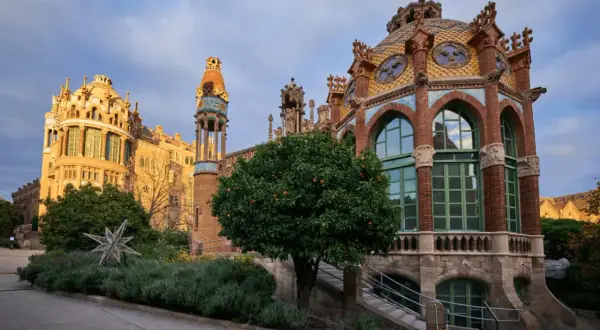 Edificios modernistas con cúpulas coloridas y arcos, rodeados de vegetación y un árbol frutal.