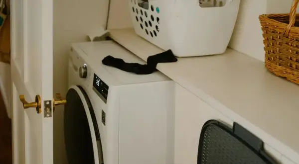 Lavadora blanca lista para instalar. Cesta de ropa y cesto de mimbre en la repisa superior.