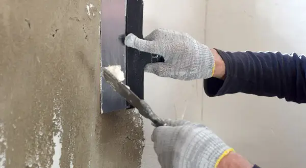 Manos enguantadas aplican yeso para sanear pared con llana.