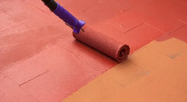 Rodillo morado pintando un suelo de baldosas con pintura roja, renovando el espacio.