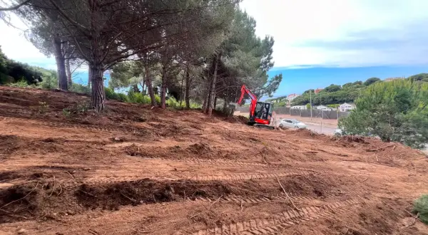 Excavadora roja trabaja en un solar urbano despejado, listo para construir.