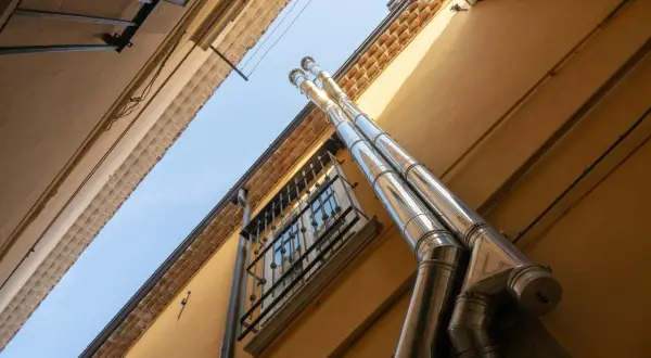 Dos tubos de acero inoxidable suben por la fachada amarilla de un edificio, parte del esquema bajantes edificio. Una ventana con rejas se ve debajo.