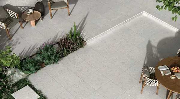 Terraza moderna con mobiliario de exterior y vegetación. El suelo está cubierto por un elegante **azulejo rectificado** de tonos grises, creando un espacio acogedor.