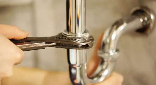 Mano ajustando tubería cromada con llave inglesa, parte de un arqueta sifónica esquema.