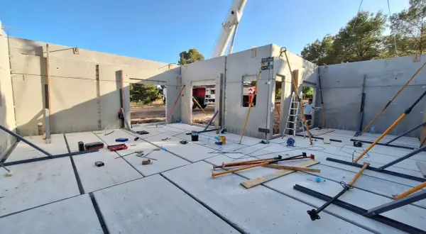Construcción de casa con paneles prefabricados. Se ve el suelo de hormigón, paredes levantadas y herramientas. ¿Cuánto cuesta terminar una casa en obra?
