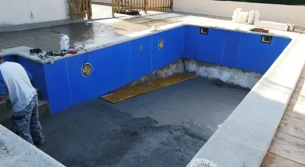 Piscina en construcción, paredes azules listas para recibir el gresite. Herramientas y materiales a un lado.