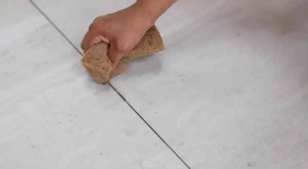 Mano aplicando lechada a las juntas de baldosas. Elige entre diversos colores de lechada para juntas para un acabado perfecto.