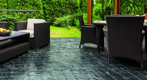 Terrazas con suelo de piedra oscura, muebles de mimbre y vegetación exuberante.