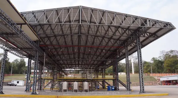 Estructura metálica de gran tamaño con cubiertas estructurales que albergan equipos industriales y tuberías.