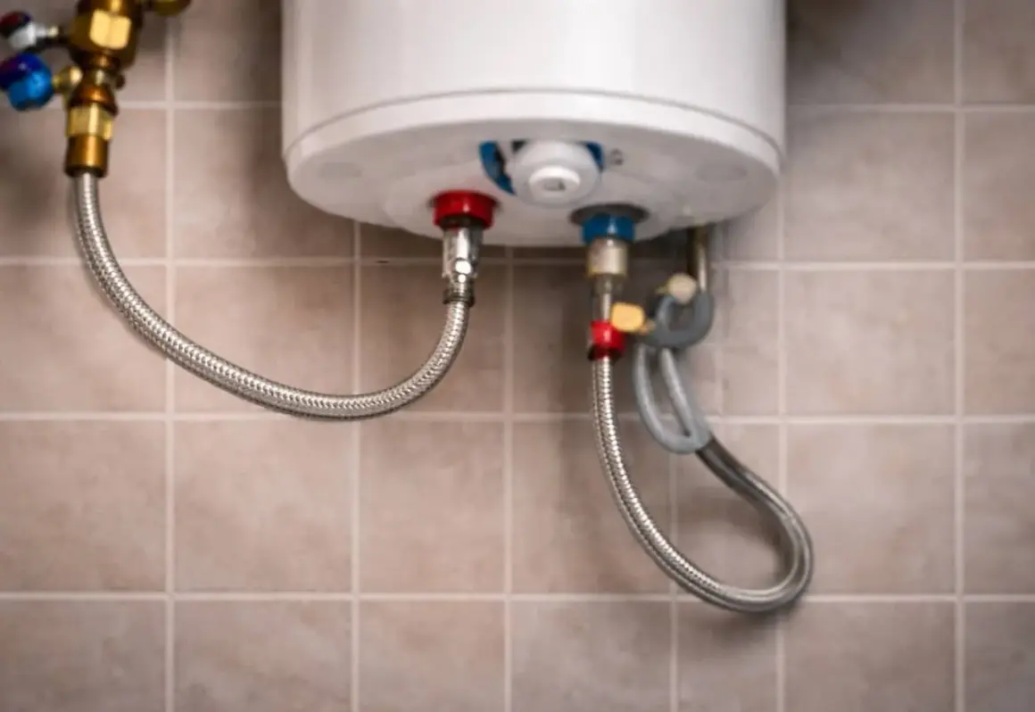 Detalle de la instalación de fontanería de un calentador de agua, con mangueras flexibles conectadas a las tomas de agua.