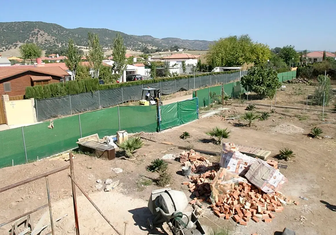 Terreno con materiales para construir dos casas. Se ven ladrillos, cementera y una excavadora.