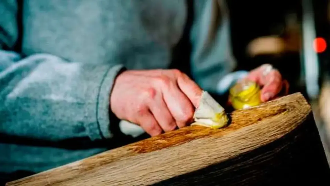 Manos aplicando cera a un trozo de madera. El proceso de **decapar madera** revela su belleza natural.