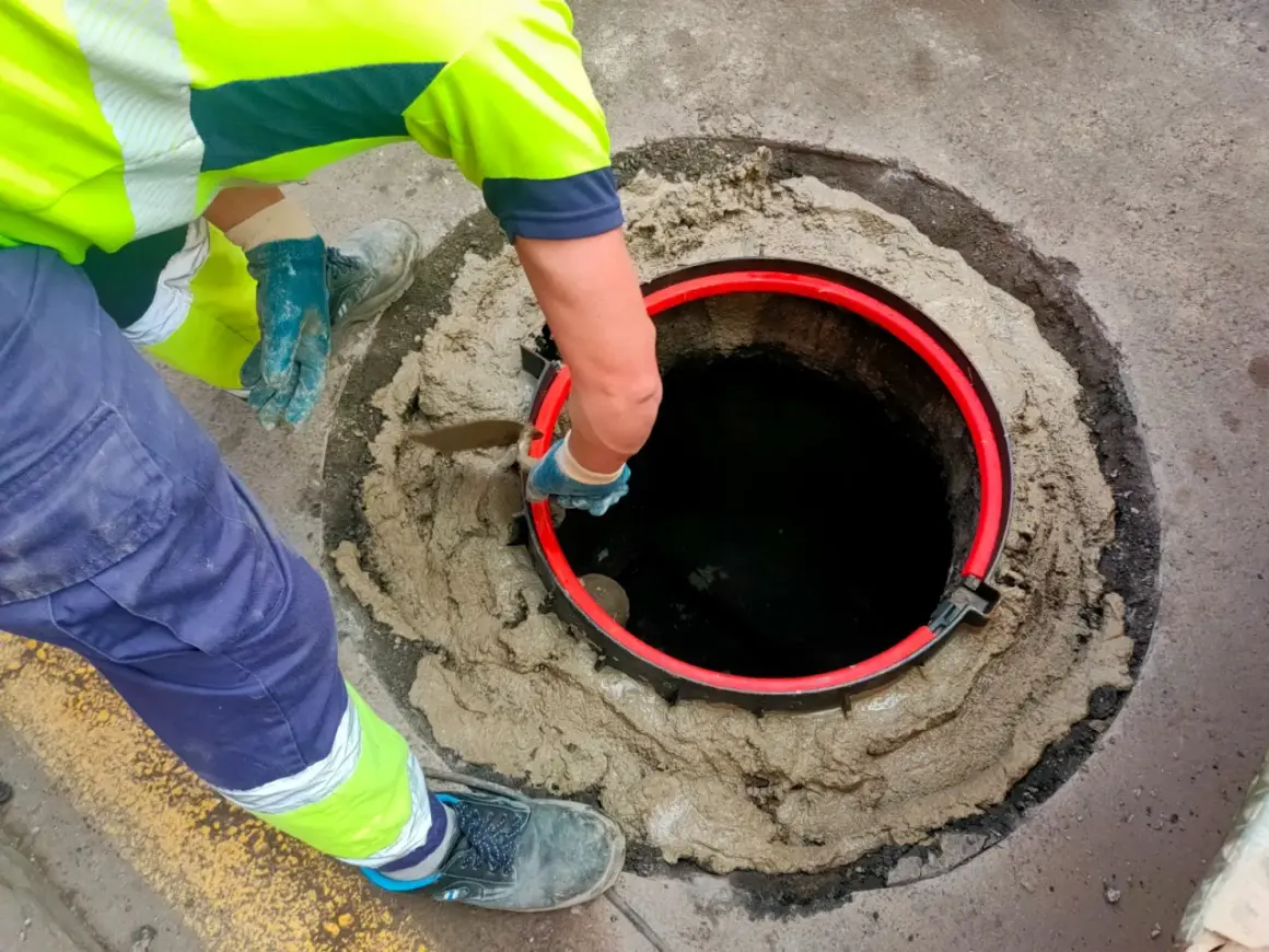 Trabajador instala un anillo rojo en una alcantarilla. Averigua cuanto cuesta conectarse al alcantarillado.