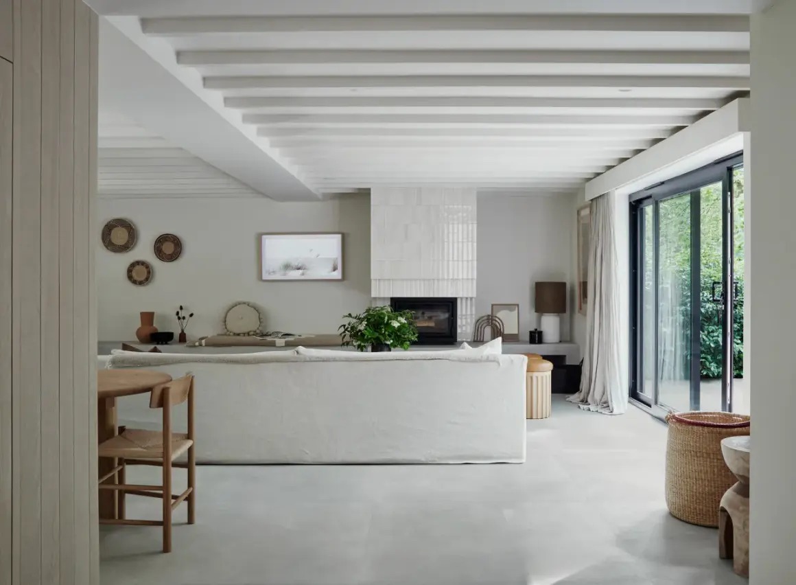 Salón moderno con suelo de porcelánico que es perfecto para crear un ambiente sereno. Sofá blanco, chimenea y grandes ventanales.