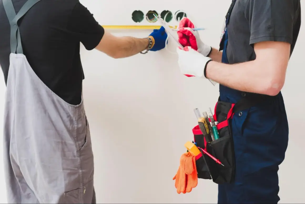 Dos electricistas trabajan en la instalación eléctrica de una vivienda, midiendo y anotando detalles.