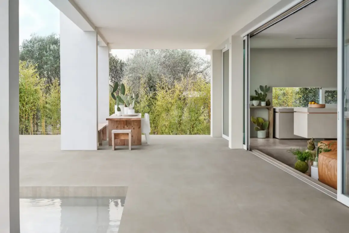 Terraza moderna con mesa de madera y cactus, sobre un impecable suelo gres que se extiende hasta una piscina.