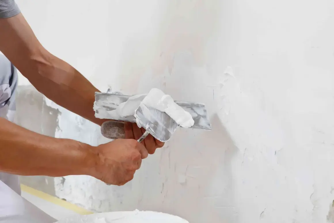 Man aplicando yeso a una pared con una llana, mostrando la diferencia entre enfoscado y guarnecido.