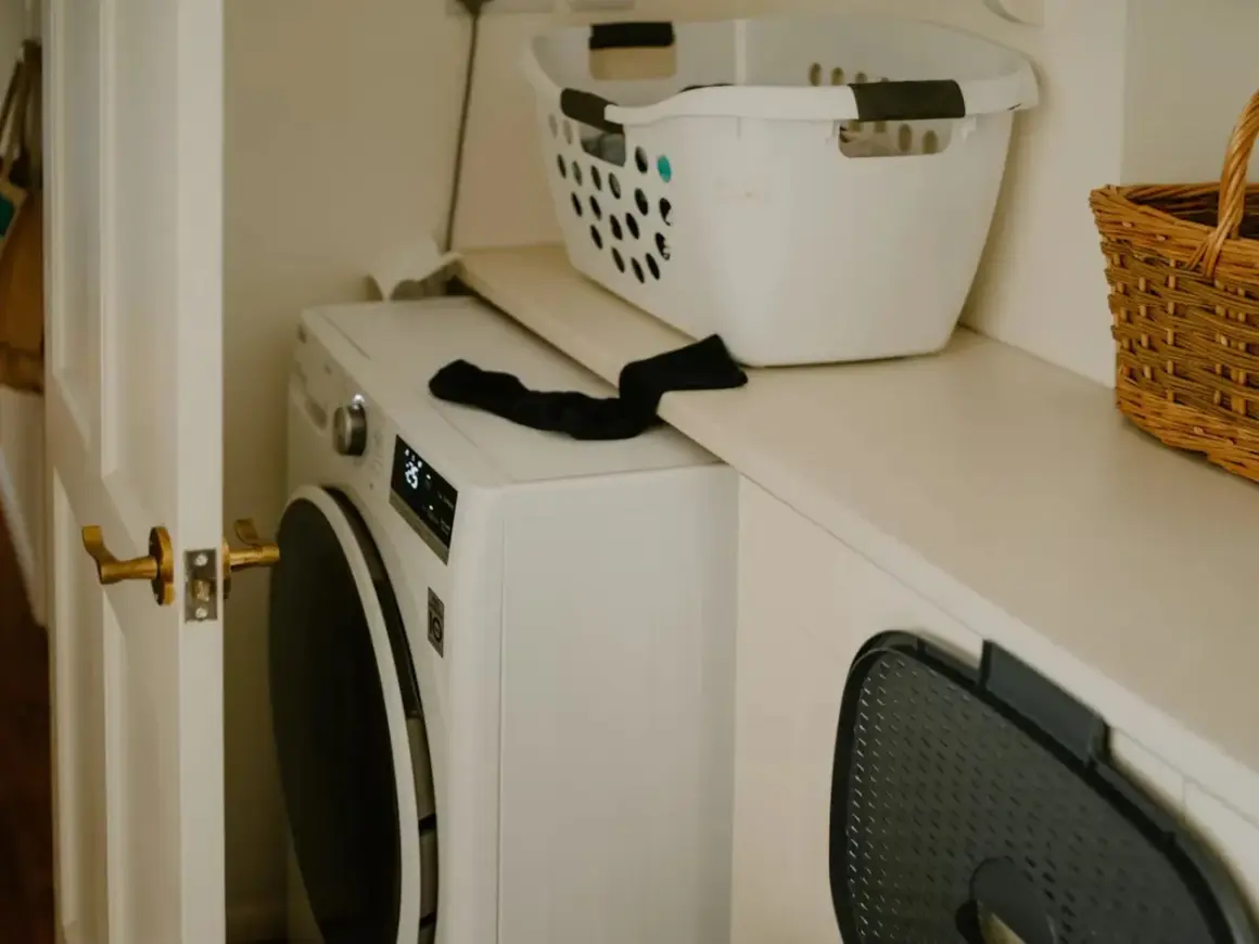 Lavadora blanca lista para instalar. Cesta de ropa y cesto de mimbre en la repisa superior.