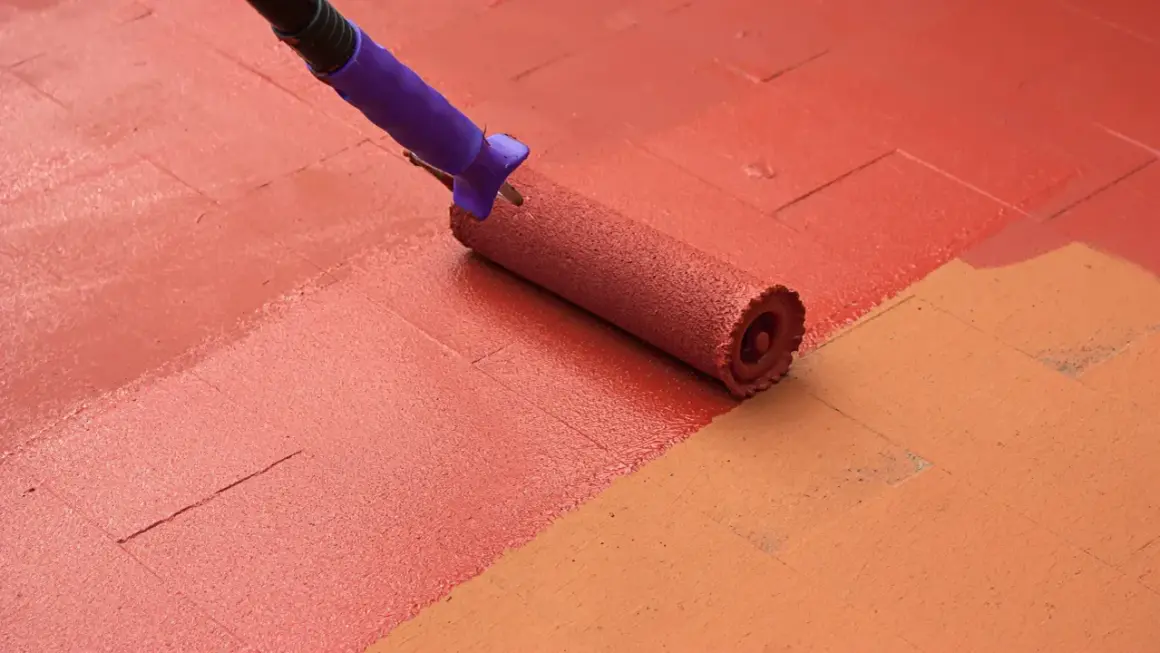 Rodillo morado pintando un suelo de baldosas con pintura roja, renovando el espacio.