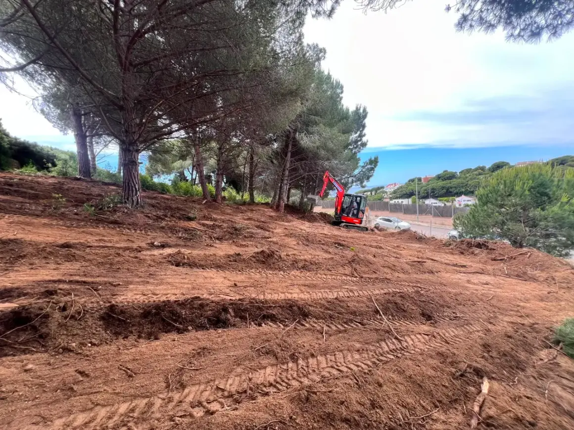 Excavadora roja trabaja en un solar urbano despejado, listo para construir.