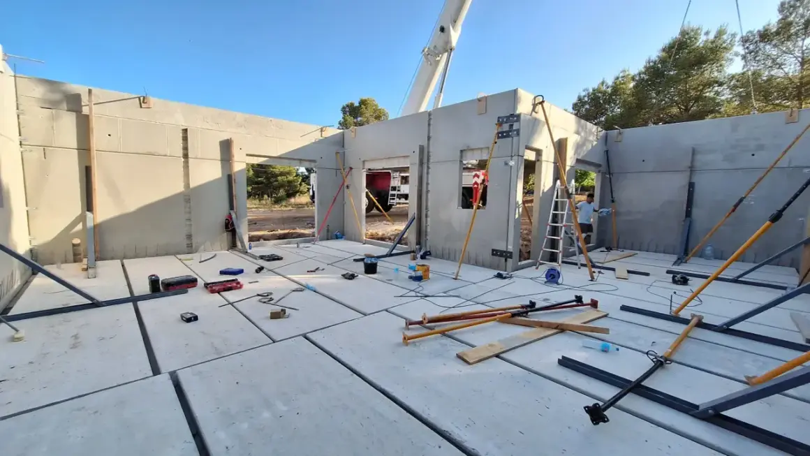 Construcción de casa con paneles prefabricados. Se ve el suelo de hormigón, paredes levantadas y herramientas. ¿Cuánto cuesta terminar una casa en obra?