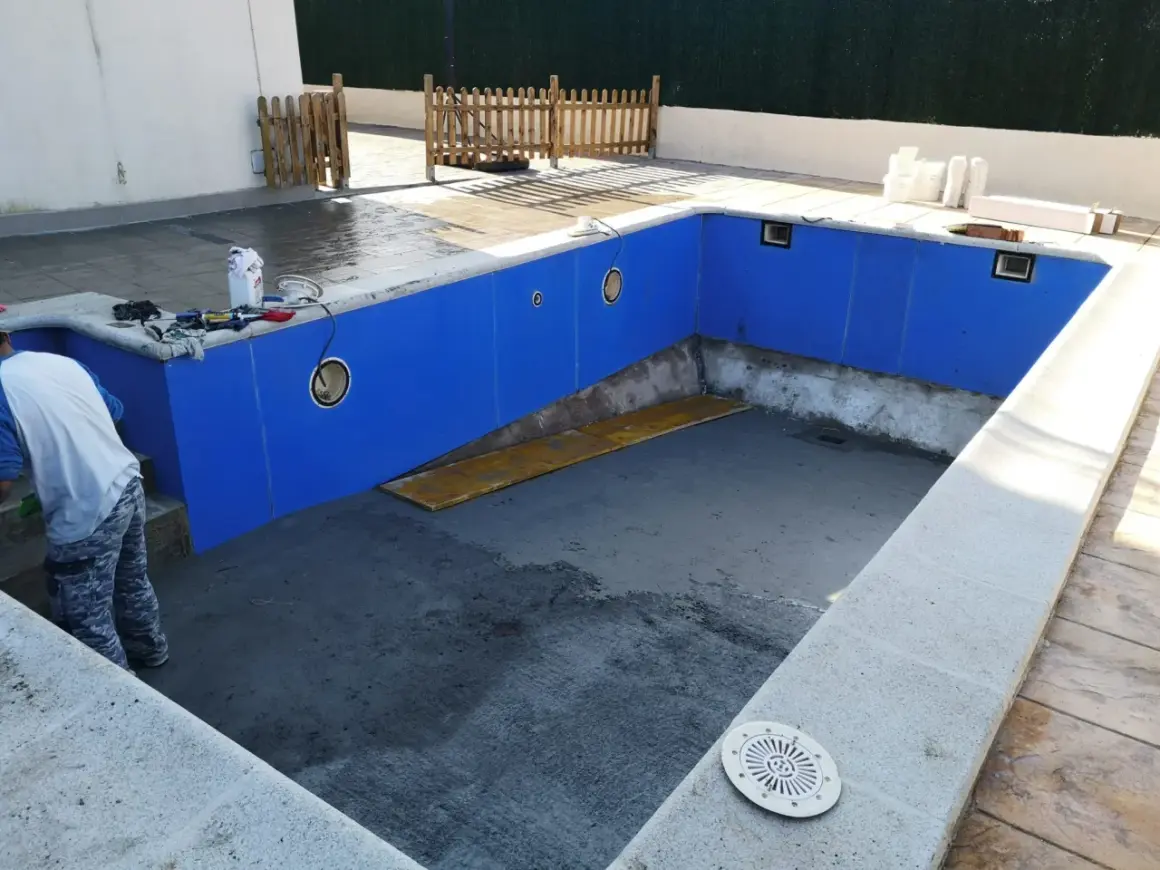 Piscina en construcción, paredes azules listas para recibir el gresite. Herramientas y materiales a un lado.