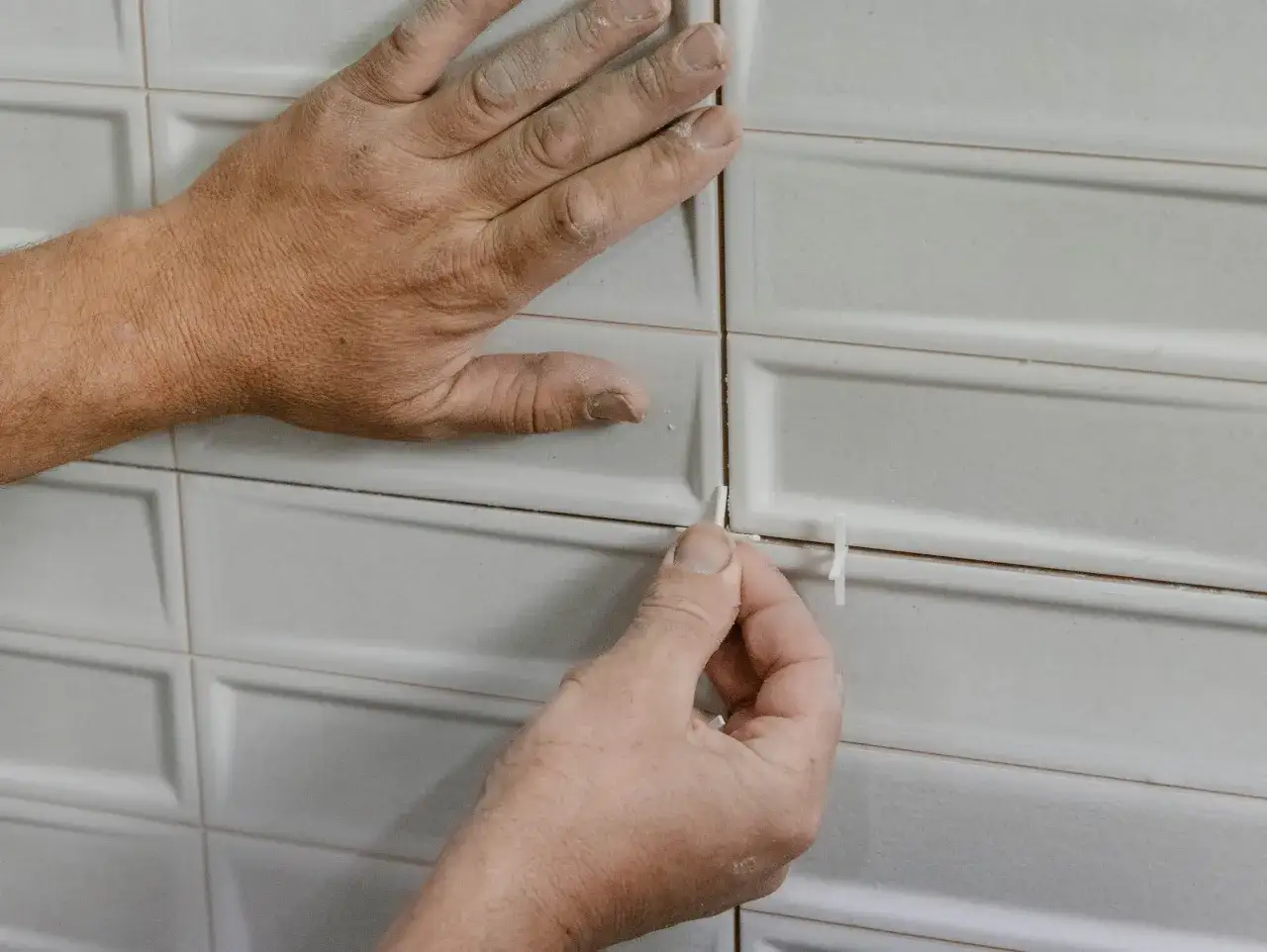 Manos colocando cu&ntilde;as en las juntas de un azulejo rectificado blanco para asegurar un acabado perfecto.