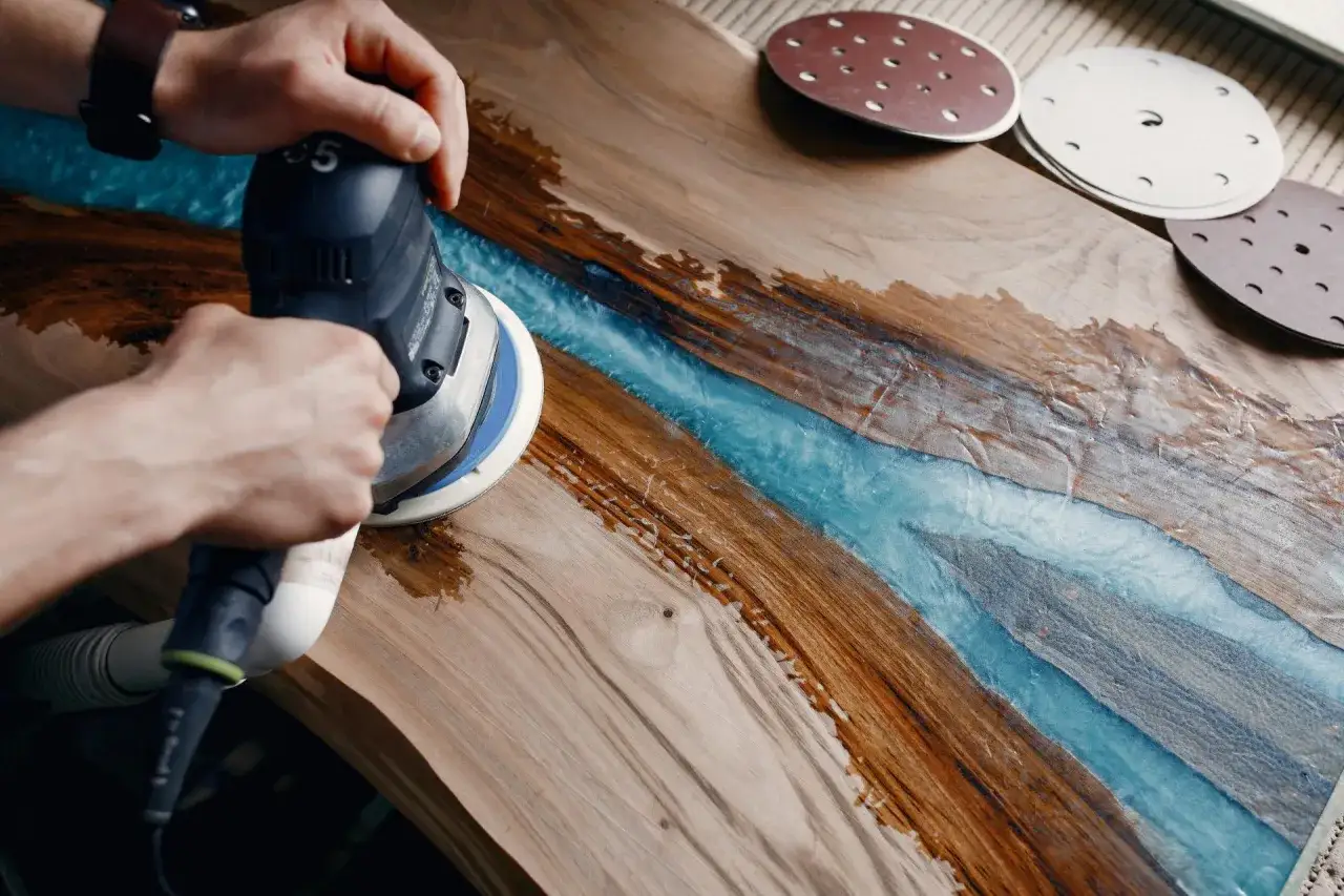 Manos lijando una mesa de madera con resina azul. El proceso de decapar madera revela la belleza natural de la veta.