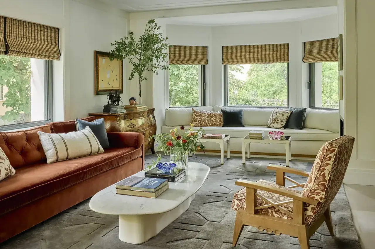 Un sal&oacute;n elegante con sof&aacute;s, mesa de centro de m&aacute;rmol y una silla de dise&ntilde;o, obra de decoradores de interiores que combinan texturas y colores.