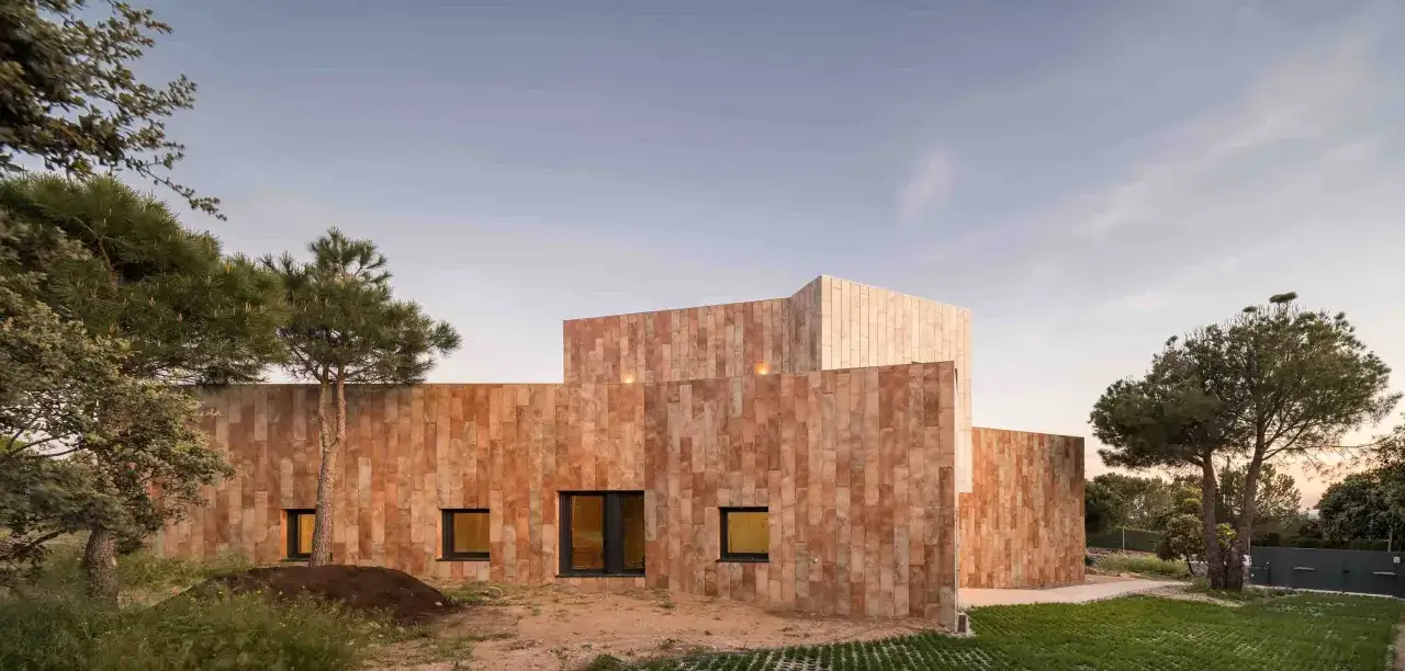 Edificio moderno con paredes porcelanico para fachadas exteriores, rodeado de &aacute;rboles y vegetaci&oacute;n bajo un cielo despejado.