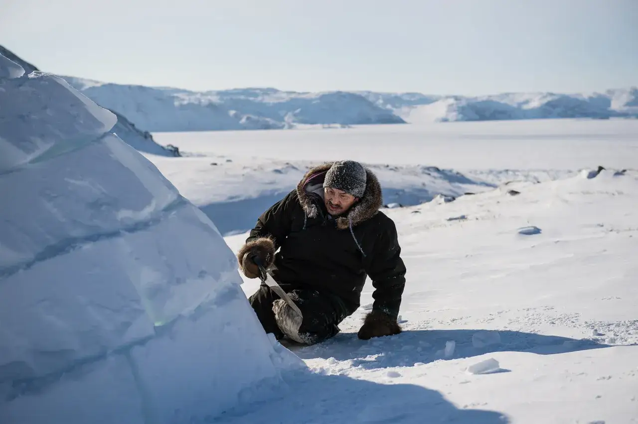 Hombre con abrigo de piel talla bloques de hielo para construir casas en el polo norte. Paisaje nevado y helado.