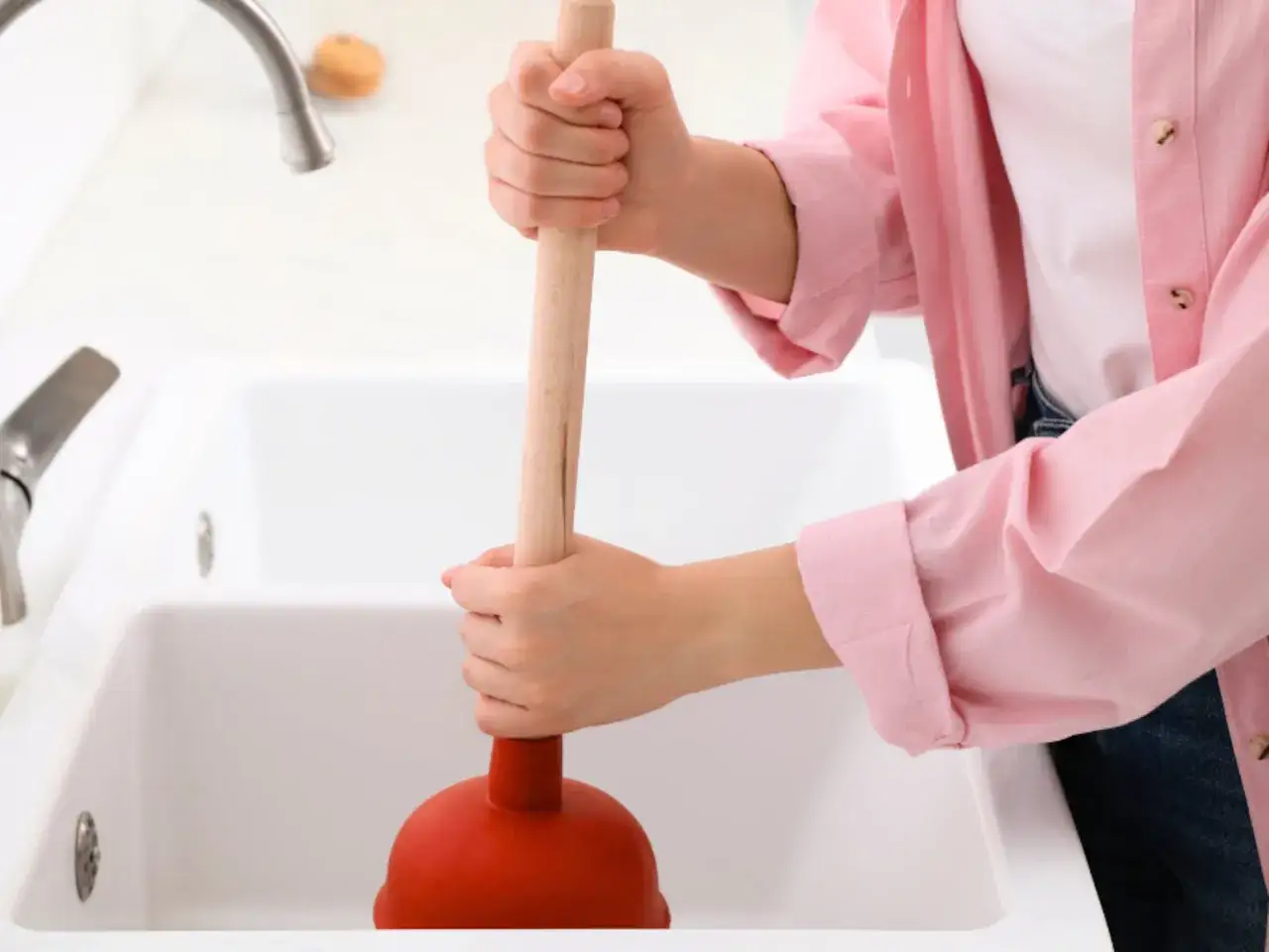 Persona usa un desatascador para solucionar un atasco en la tuber&iacute;a del lavabo.