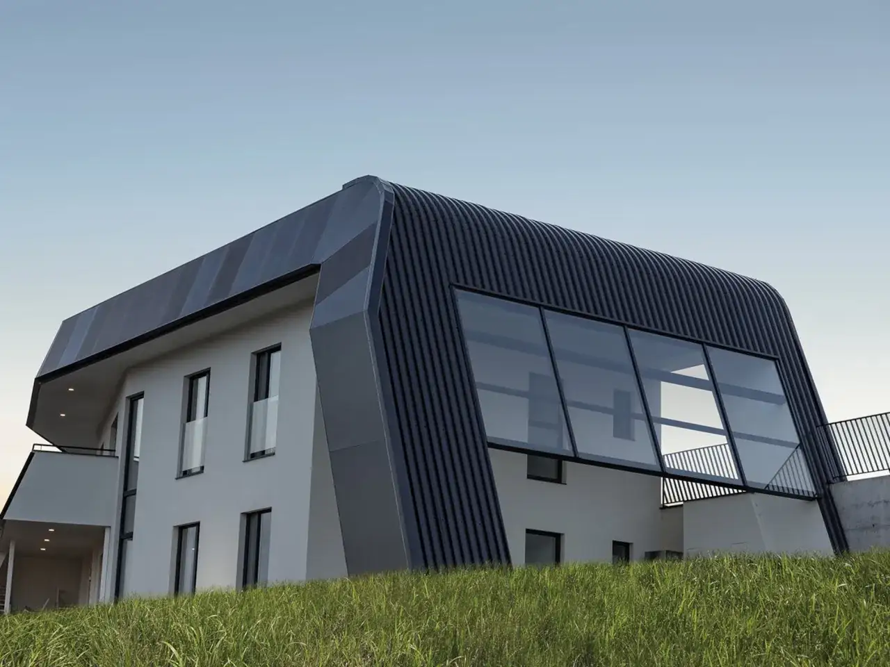 Moderna casa ecol&oacute;gica autosuficiente con techo curvo y grandes ventanales, rodeada de hierba alta.