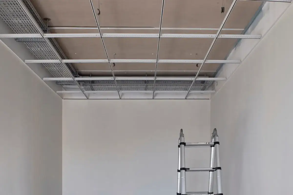 Estructura met&aacute;lica para falso techo pladur, con bandejas de cables visibles. Escalera plegable lista para continuar el trabajo.